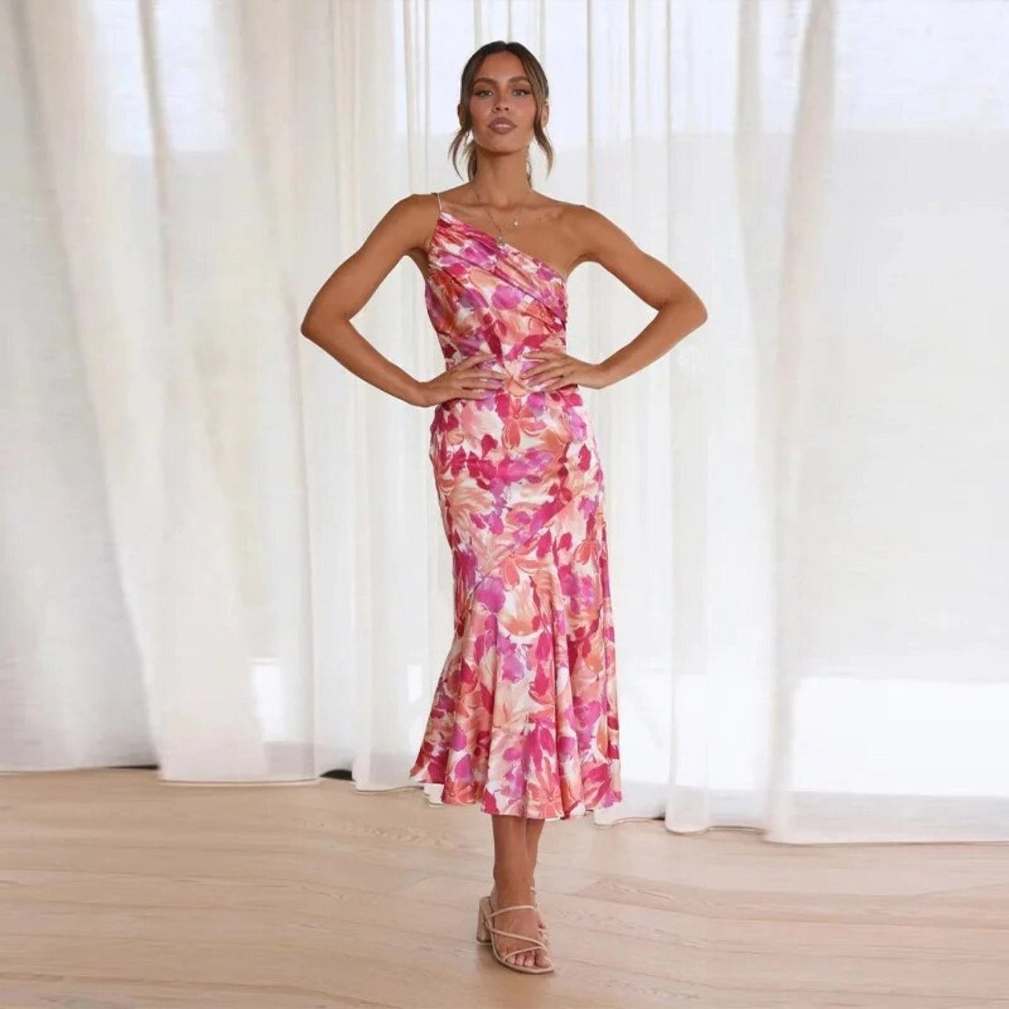 A woman wearing a one-shoulder orange floral midi dress with a fitted waist and thigh-length hem, suitable for elegant summer cocktail events.