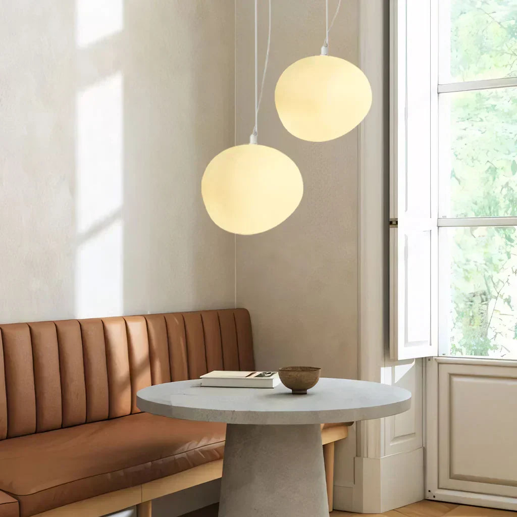 Elegant white pebble pendant light; minimal design, frosted glass, metal accents, soft glow for modern interiors.