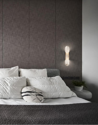 "Modern elongated alabaster wall lamp with metal and brass accents, emits warm glow, suitable for chic interior decor."