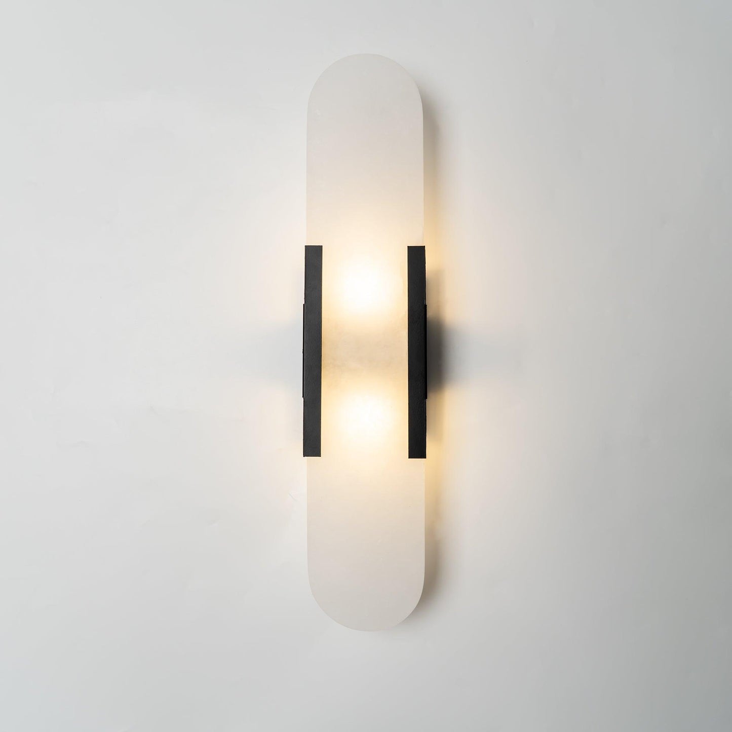 "Modern elongated alabaster wall lamp with metal and brass accents, emits warm glow, suitable for chic interior decor."