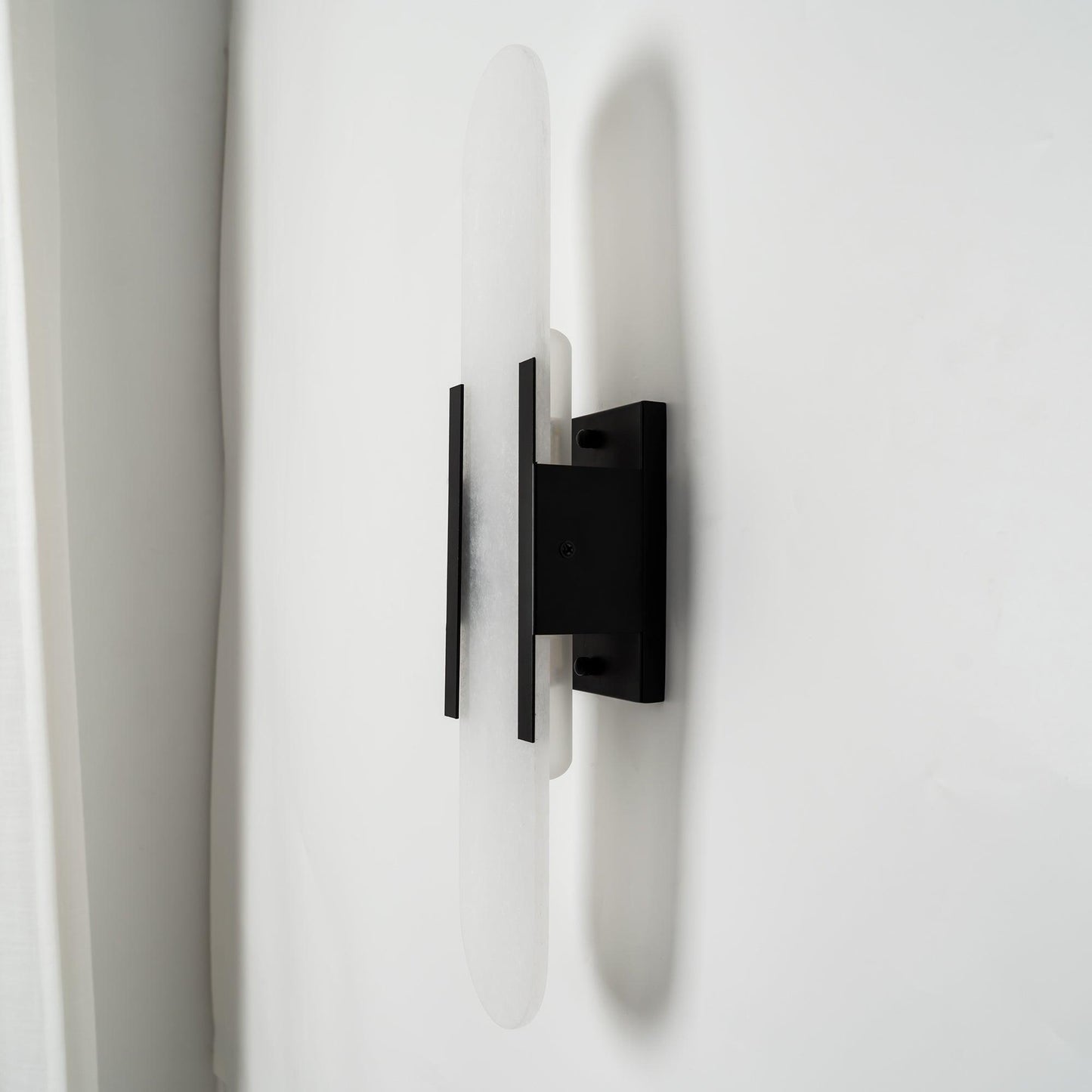 "Modern elongated alabaster wall lamp with metal and brass accents, emits warm glow, suitable for chic interior decor."