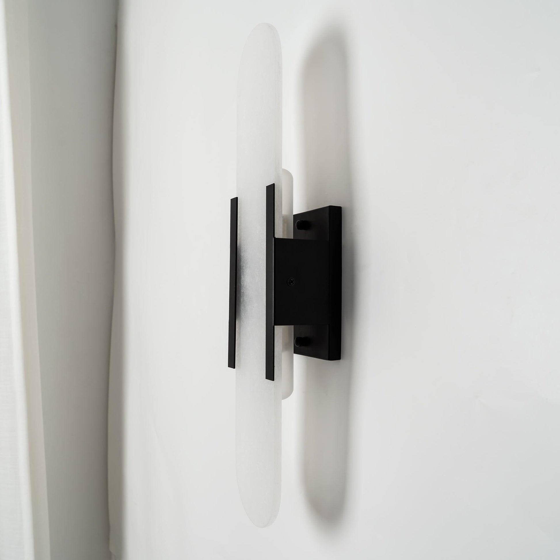 "Modern elongated alabaster wall lamp with metal and brass accents, emits warm glow, suitable for chic interior decor."
